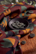 Gros plan sur l'imprimé floral graphique aux formes de feuilles du tissu Seraphine bordeaux, moutarde et sauge.