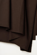 Gros plan sur les plis verticaux serrés du tissu gabardine légère marron chocolat.