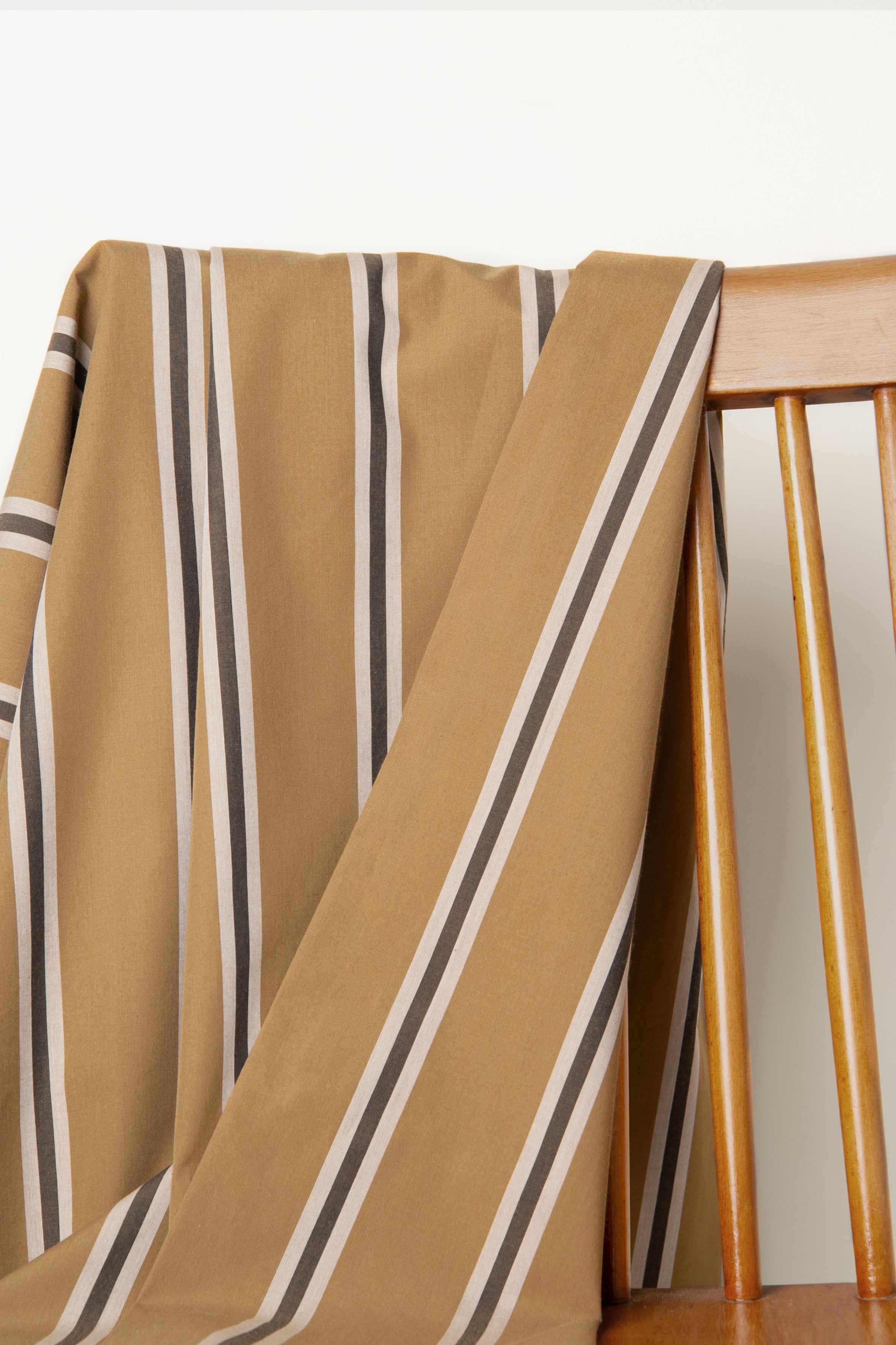 Weave Line fabric, caramel with vertical charcoal grey and off-white stripes, draped over the back of a wooden chair.