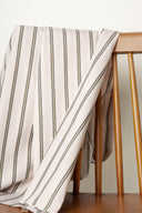 Tissu Weave Line écru à rayures verticales kaki et anthracite, drapé sur le dossier d'une chaise en bois.