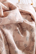 Tissu Vera rose poudré plié, avec une bobine de fil rose en bois et un bol noir contenant des boutons bordeaux.